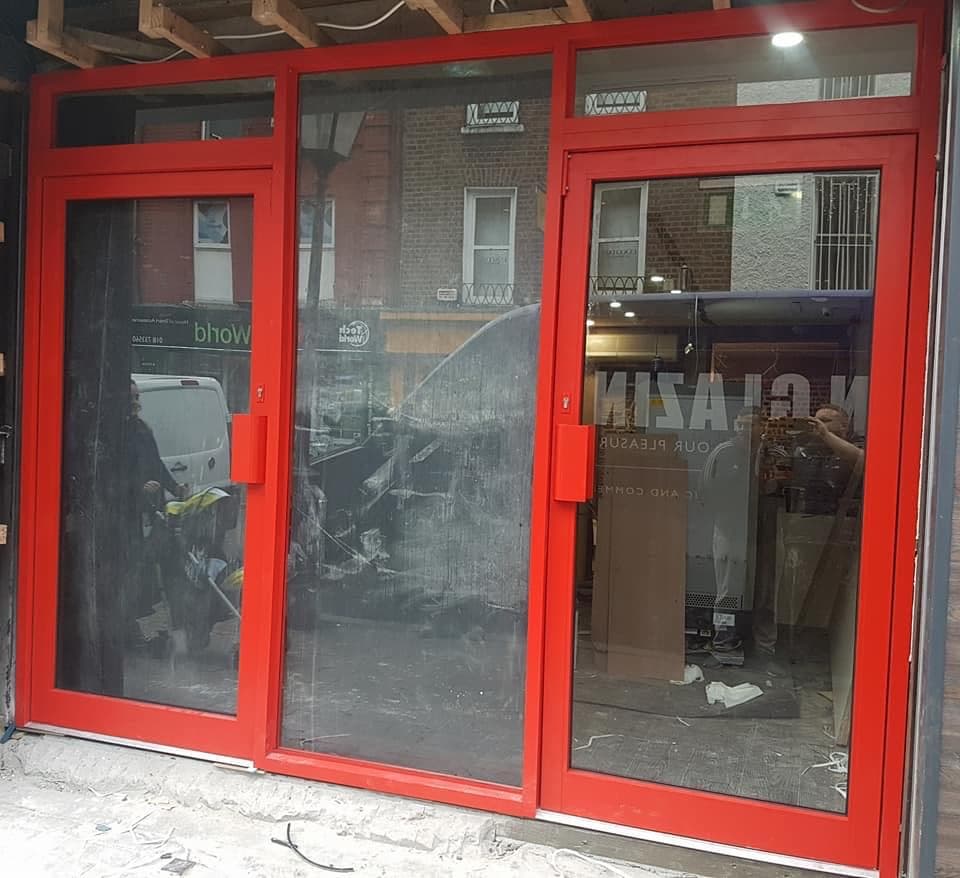 Red aluminium shopfront glazing being installed on a commercial unit