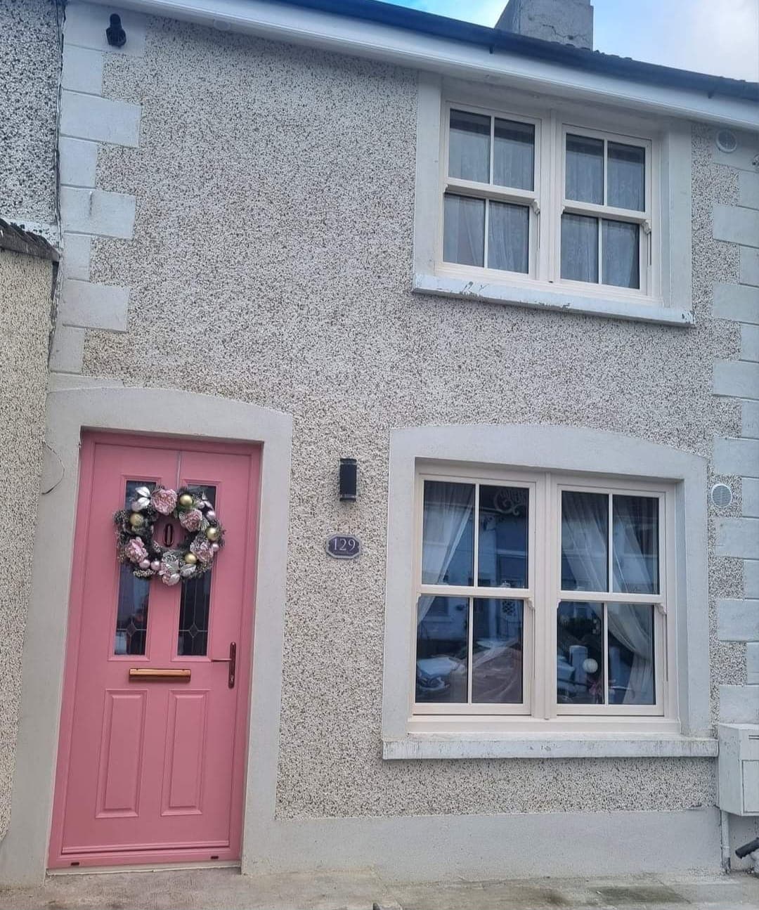 Cream sash windows and a pink composite front door on a pebbledash terraced house